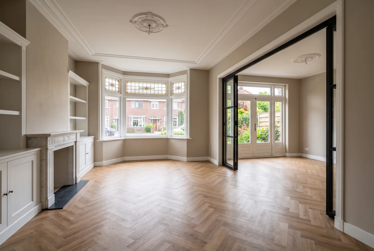 Lege woonkamer van een jaren-30-woning: erker, schouw en suitedeuren