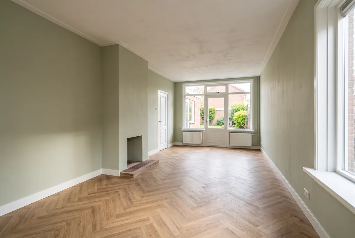 Lege woonkamer van een jaren-70-doorzonwoning: licht van twee kanten, haard op de lange wand