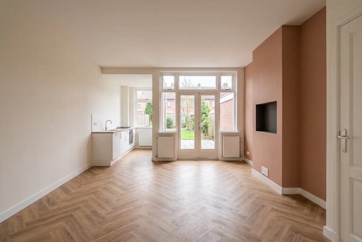 Lege woonkamer van een jaren-90-woning: pui met openslaande deuren, schouw met tv-plek