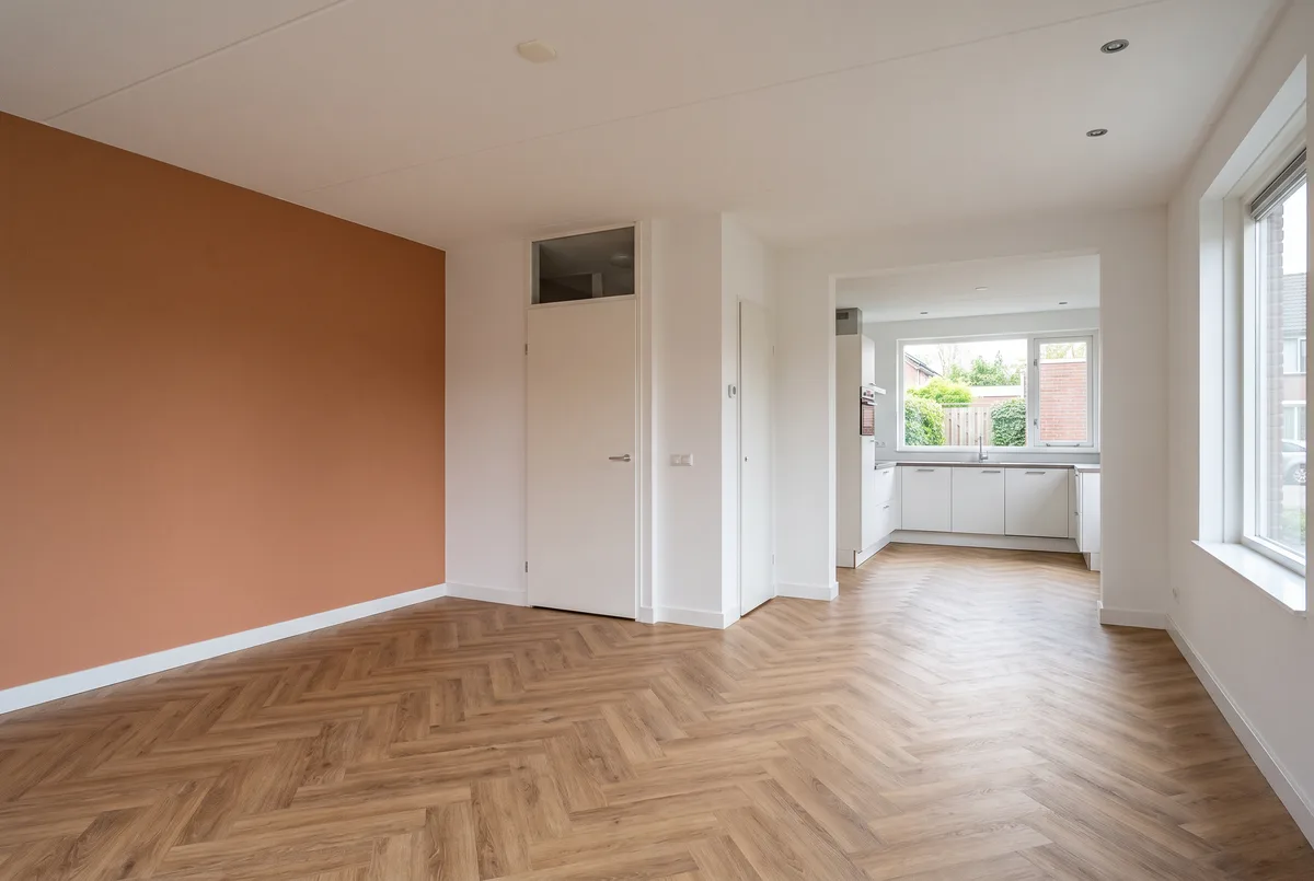 Lege woonkamer van een u-woning jaren 90/2000: zithoek voor, open keuken achter, trap en toilet ertussen